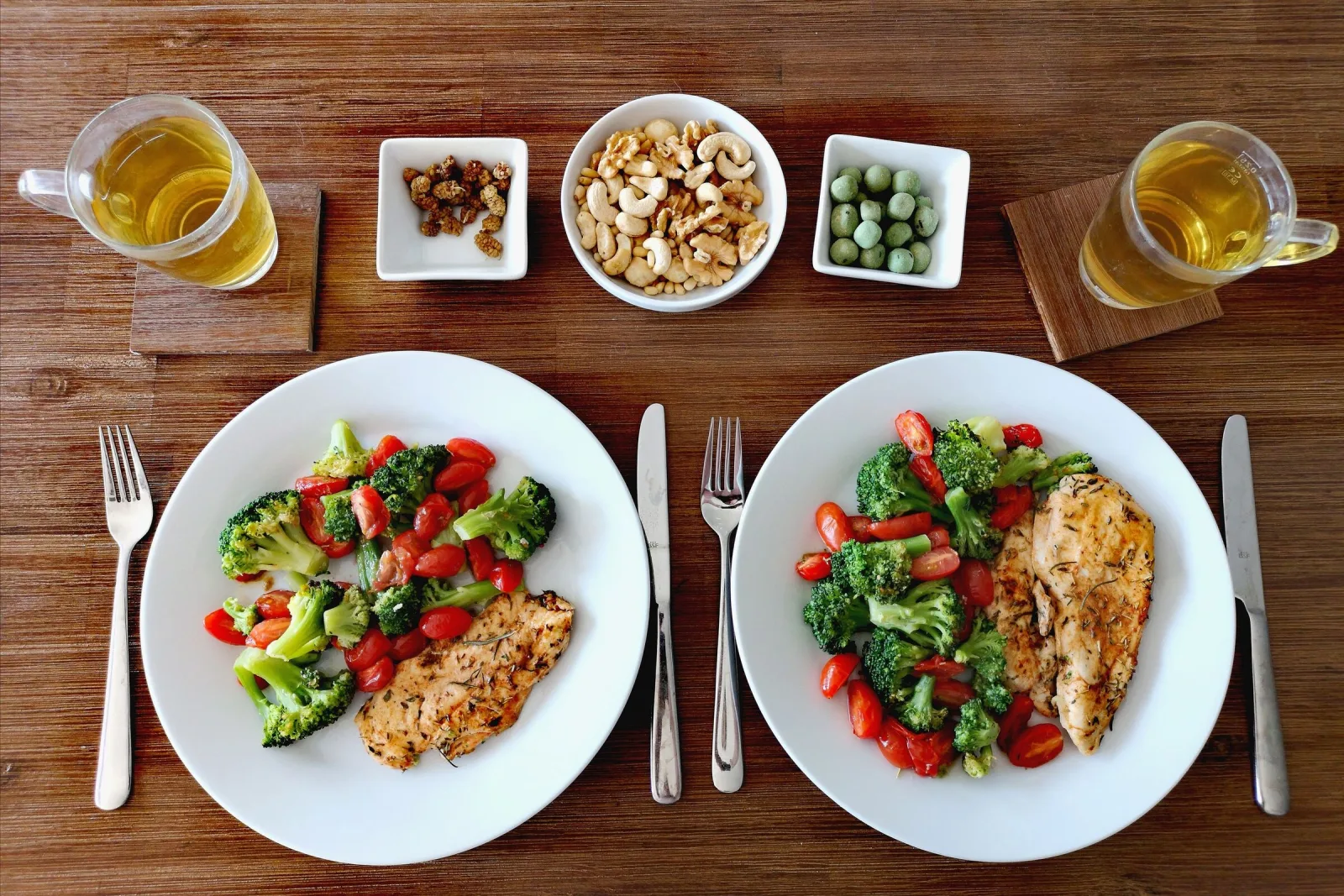 Ahşap masada ızgara tavuk ve sebzeli iki tabak, yanında kuruyemiş ve bitki çayı